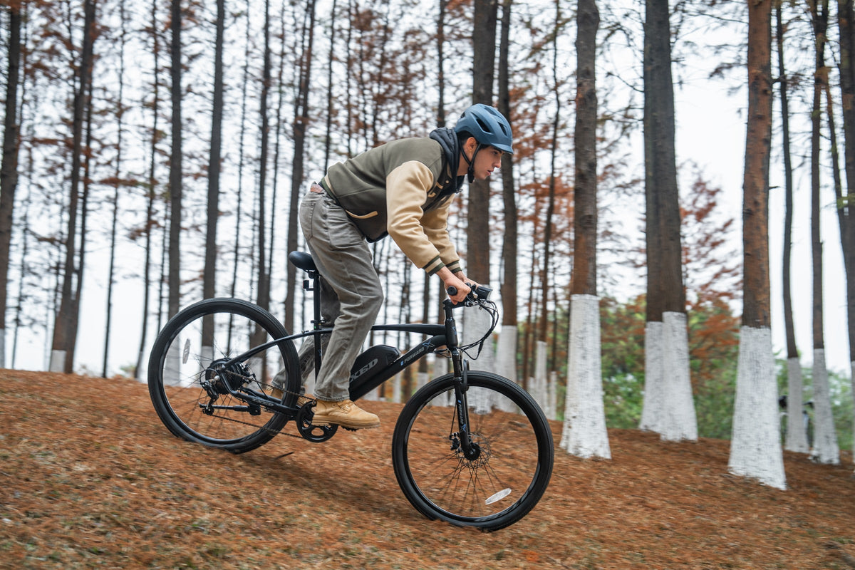 Helmeted rider on a TXED Trail electric bike on a wooded dirt path.